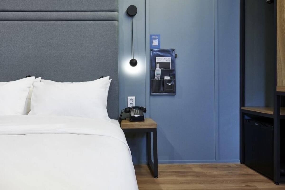 Habitació d'hotel amb un llit, una taula de nit amb un telèfon, una estació de càrrega penjada a la paret i una petita prestatgeria.