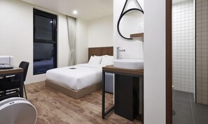 Een hotelkamer met een bed, nachtkastje en een badkamer met wastafel en spiegel.