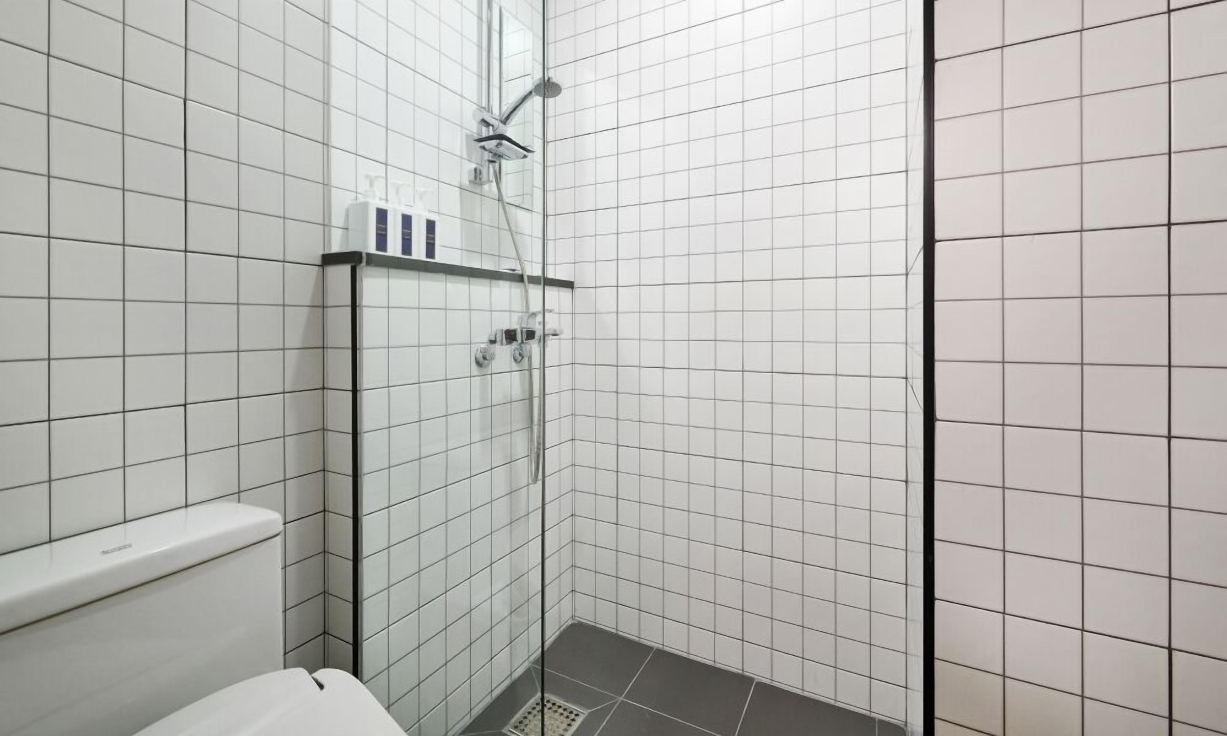 A small, tiled bathroom with a shower, toilet, and a shelf with toiletries.