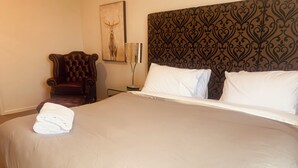 A neatly made bed with white linens, a headboard with a patterned design, a framed artwork on the wall, and a dark upholstered chair. - Cliff Hanger-Dinner Plain (Dinner Plain)
