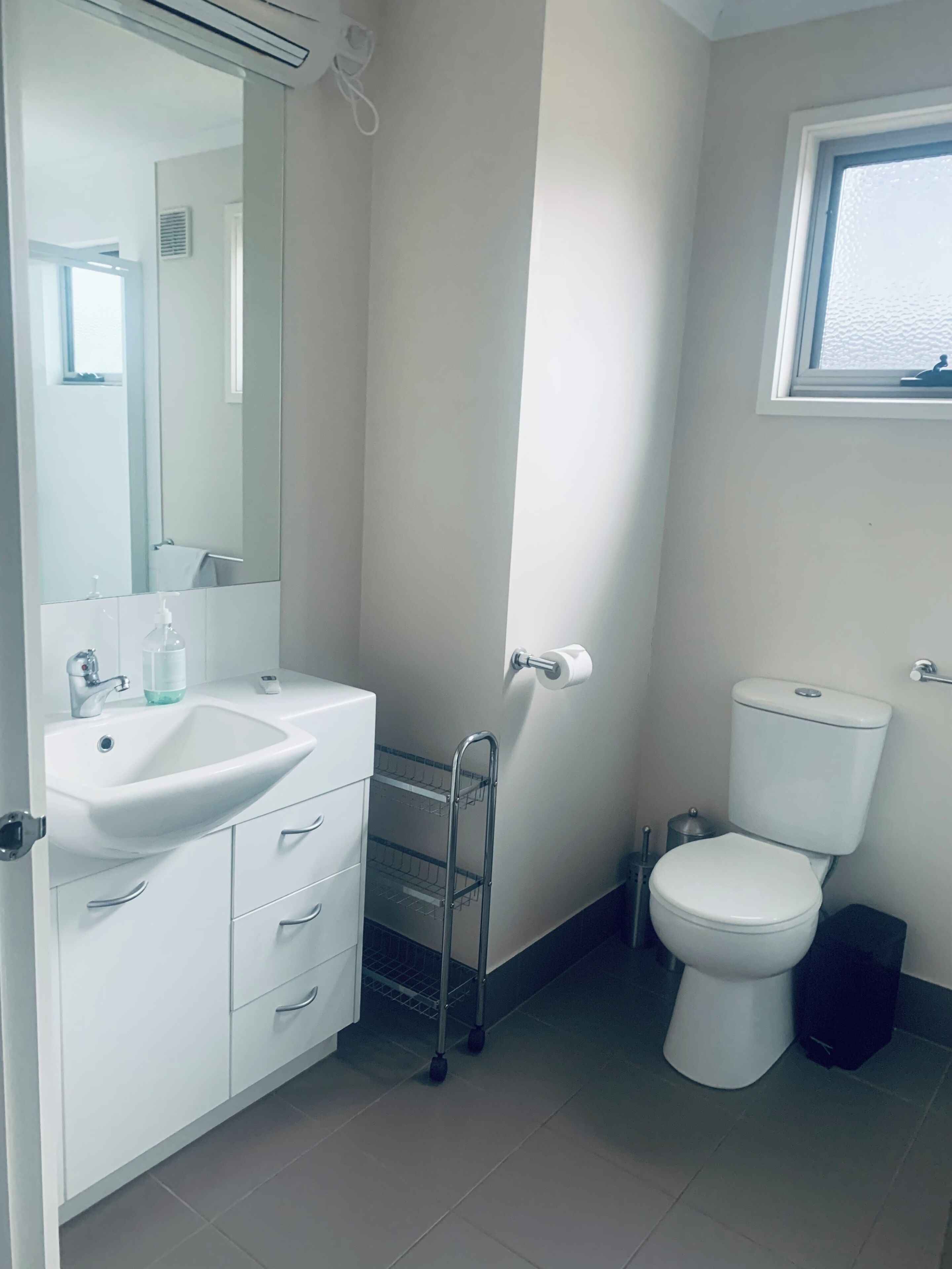 A bathroom with a white sink, mirror, toilet, and a window.