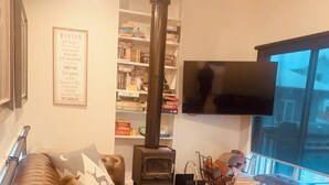 A cozy living room with a brown leather sofa, a fireplace, a bookshelf, and a flat-screen TV. - Cliff Hanger-Dinner Plain (Dinner Plain)