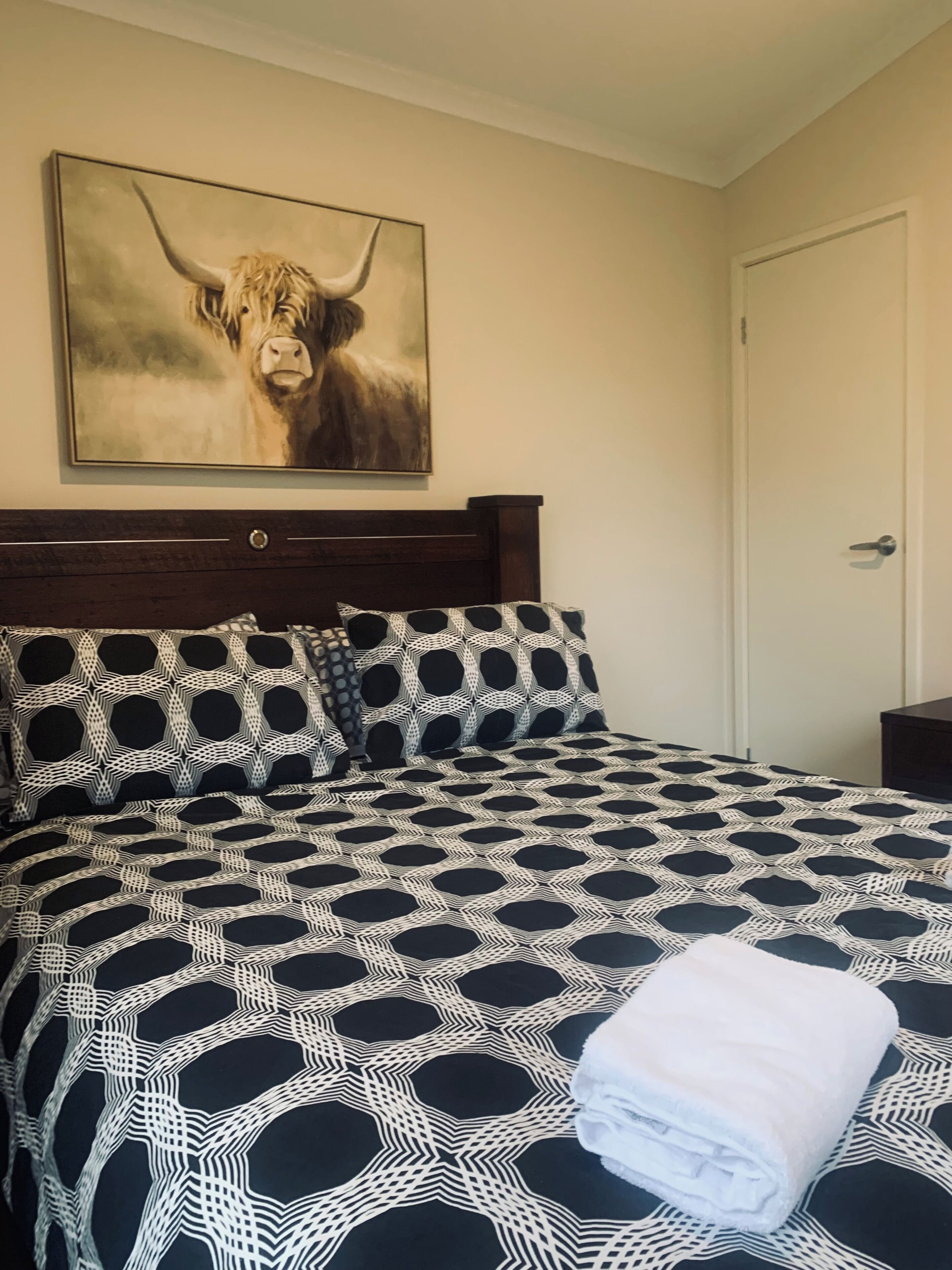 A hotel room with a large bed, a headboard, a painting of a cow, and a door.