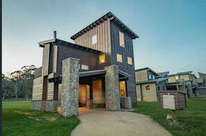 A modern two-story house with a stone foundation, a covered front porch, and a garage. - Cliff Hanger-Dinner Plain (Dinner Plain)