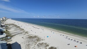 A beach with a long stretch of sand, a few umbrellas, and a few people. There are buildings along the beach. - Island Tower 1501 - Right on the Beach - Corner (Gulf Shores)