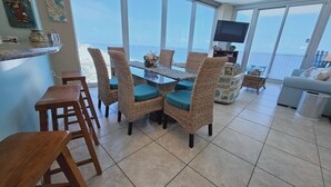 A dining area with wicker chairs and a glass table, overlooking a beach. - Island Tower 1501 - Right on the Beach - Corner (Gulf Shores)