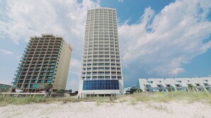 Two high-rise buildings with multiple balconies, one with a blue facade and the other with a beige facade, set against a partly cloudy sky. - Island Tower 1501 - Right on the Beach - Corner (Gulf Shores)