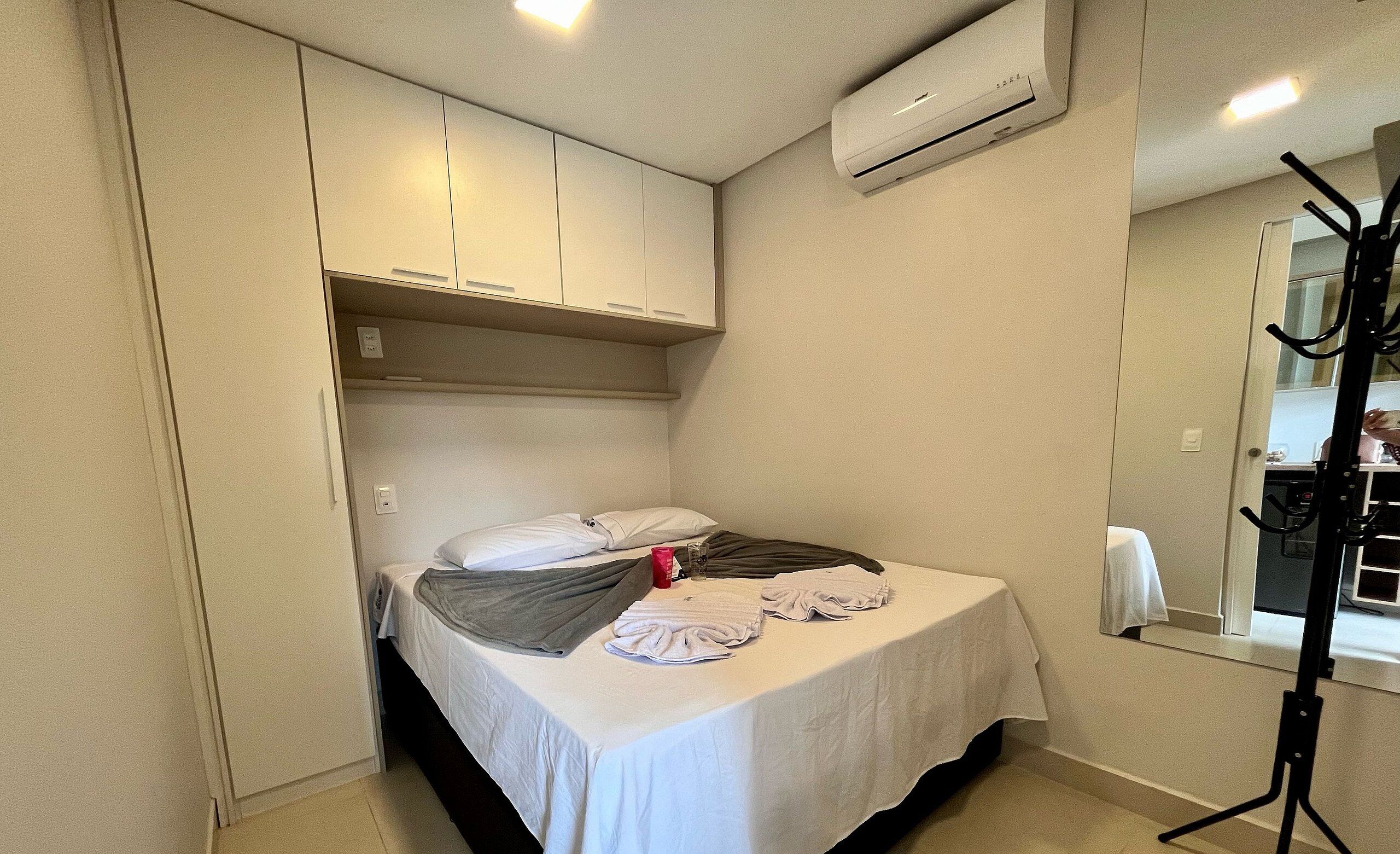 A small, neatly arranged bedroom with a bed, a mirror, and a window.