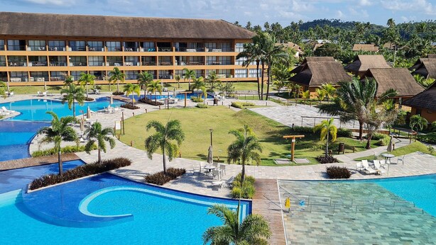 A resort with multiple swimming pools, a large building with balconies, and lush greenery.