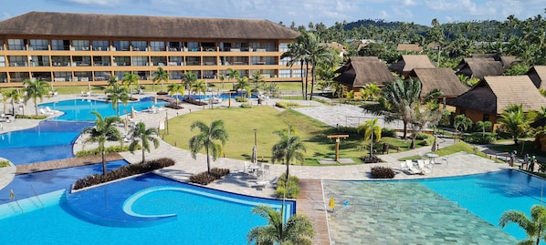 A resort with multiple swimming pools, a large building with balconies, and lush greenery.