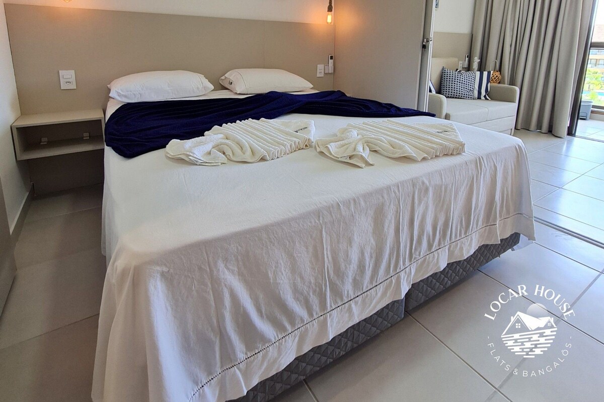 A hotel room with a bed, a wall-mounted air conditioner, and a view of the outdoors.