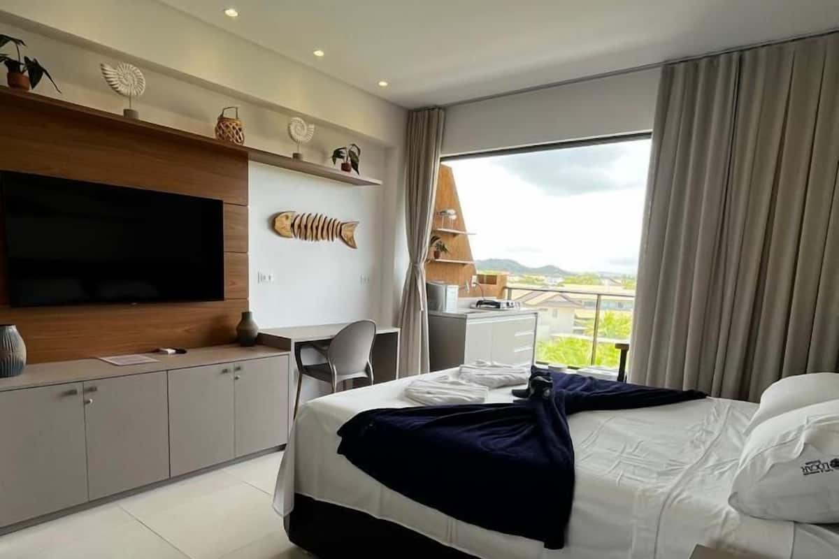 Ein modernes Hotelzimmer mit Bett, Fernseher, Schreibtisch und Blick ins Freie.