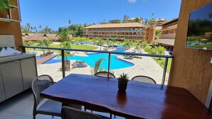 A balcony with a view of a swimming pool, a dining table, and a TV screen.