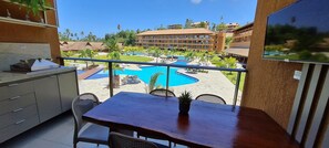 A balcony with a view of a swimming pool, a dining table, and a TV screen.
