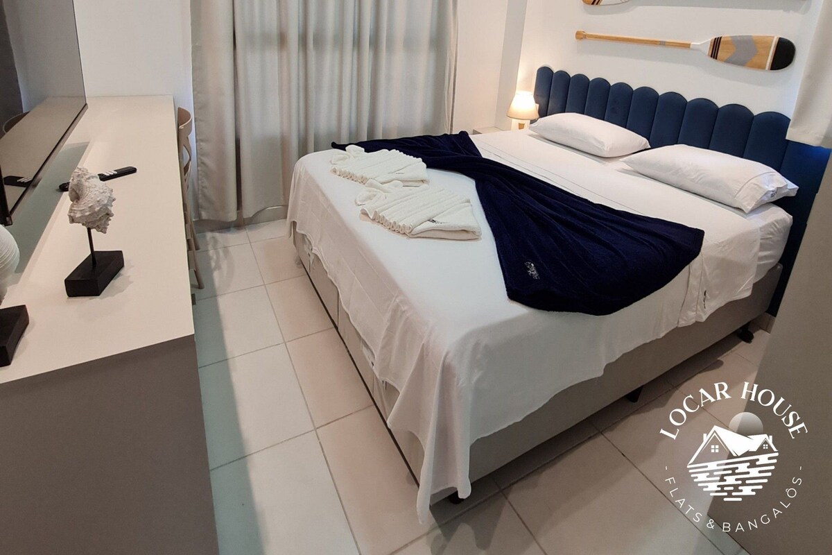 A hotel room with a bed, a desk, a lamp, and a wall-mounted paddleboard.