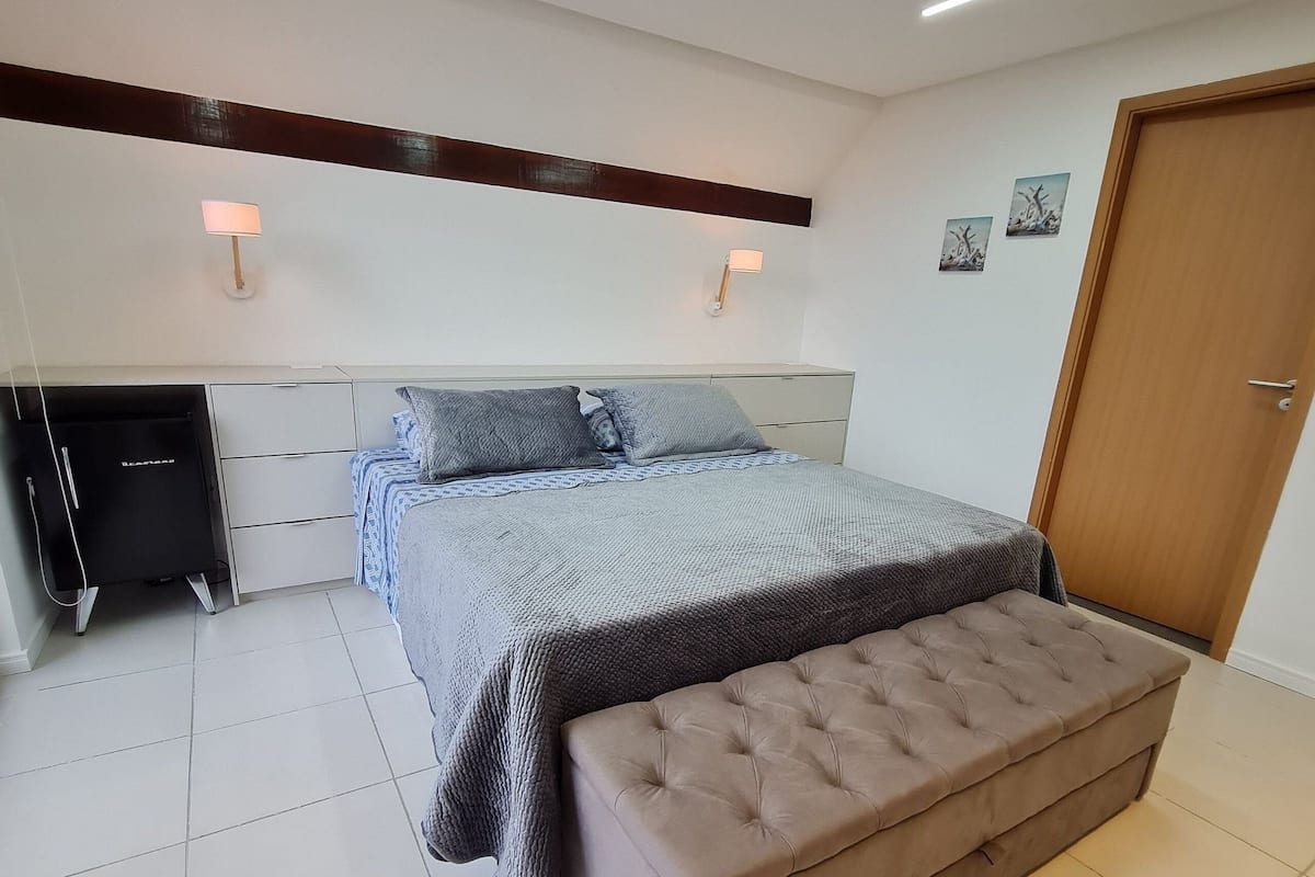 Ein Schlafzimmer mit Bett, Nachttischen, einer Bank, einem Kleiderschrank und einer Tür.