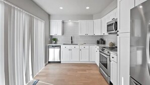 Une cuisine moderne avec des meubles blancs, des appareils en acier inoxydable et un plancher en bois.