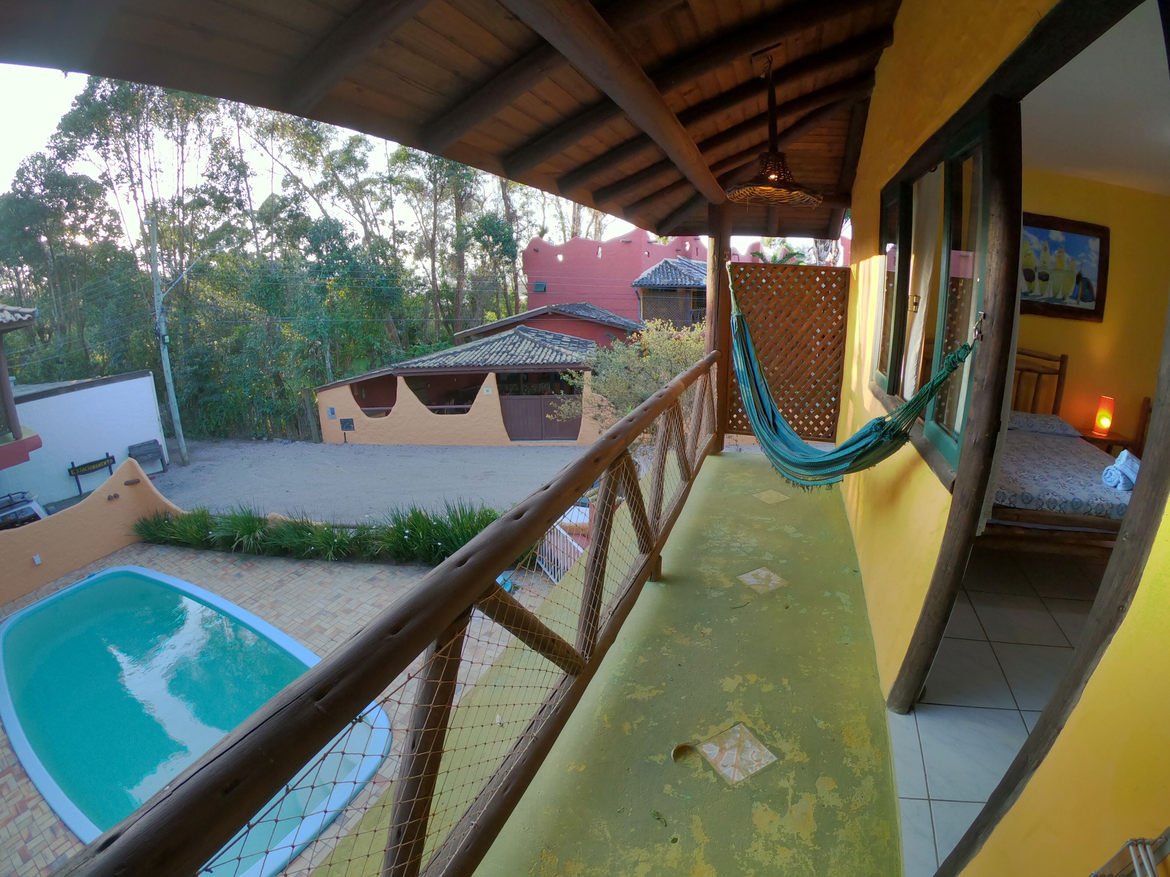 A balcony with a hammock, a pool, and a view of a house with a tiled roof.