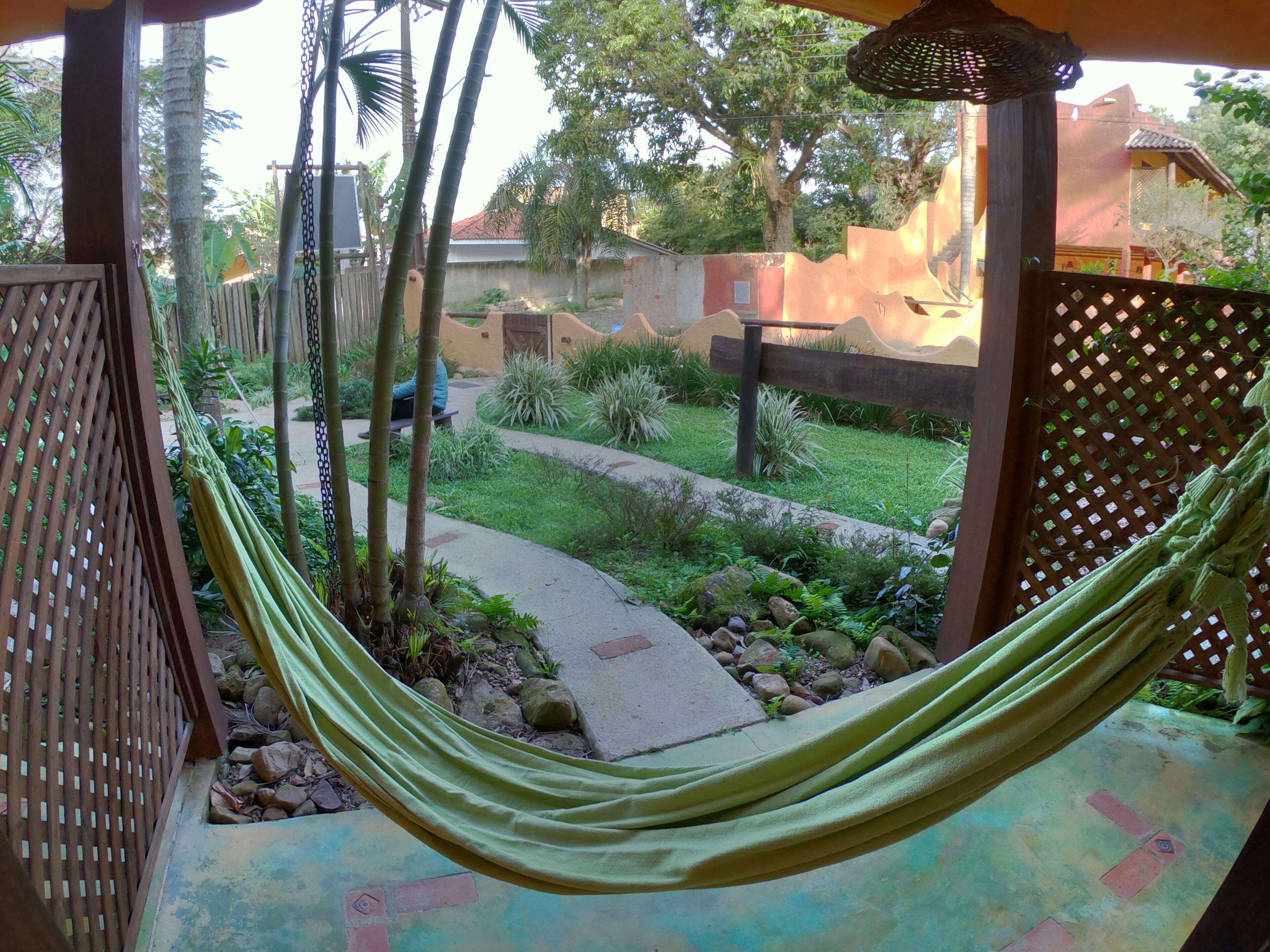 A hammock on a porch with a view of a garden and a pathway.