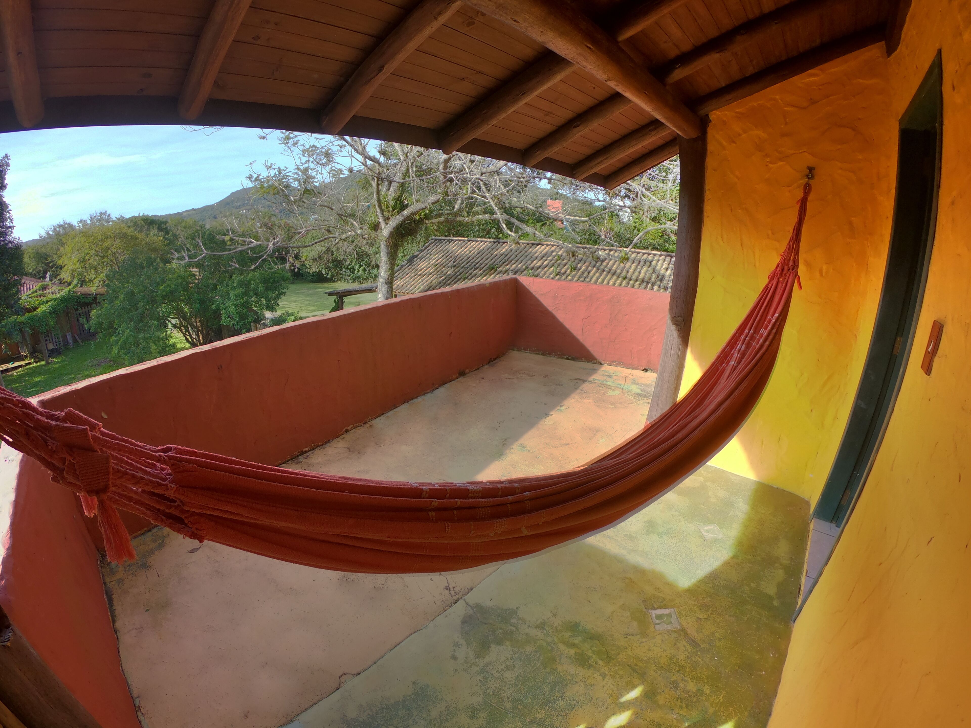 A hammock on a balcony with a view of trees and a building in the background.