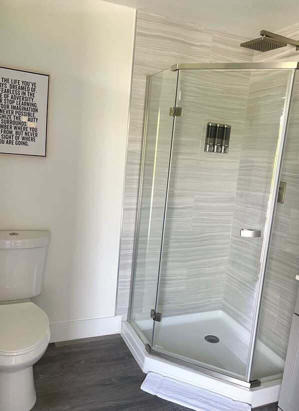 A modern bathroom with a glass-enclosed shower, a toilet, and a wall-mounted air freshener.