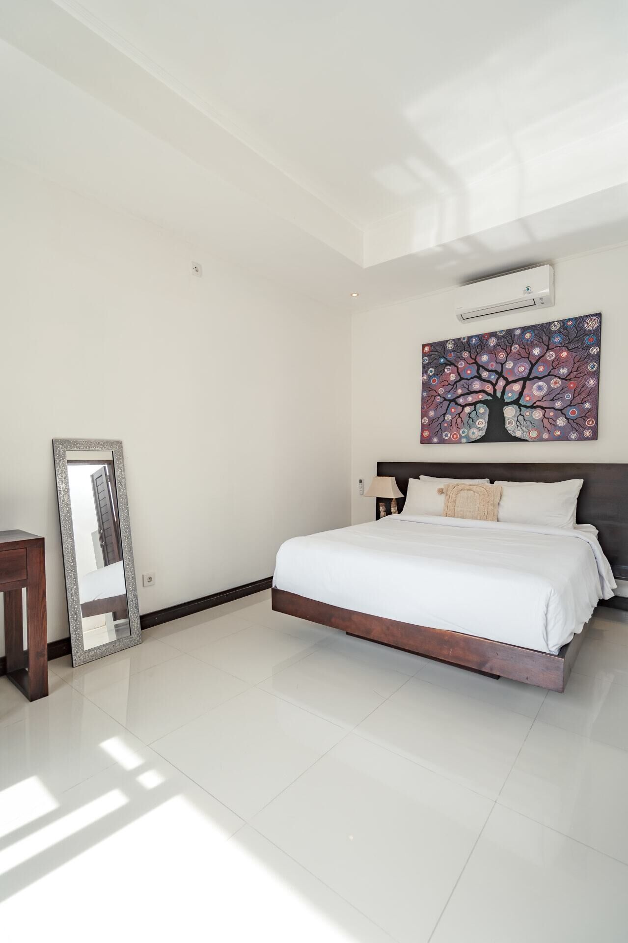 Une chambre à coucher avec un grand lit, un miroir, un tableau et un ventilateur de plafond.