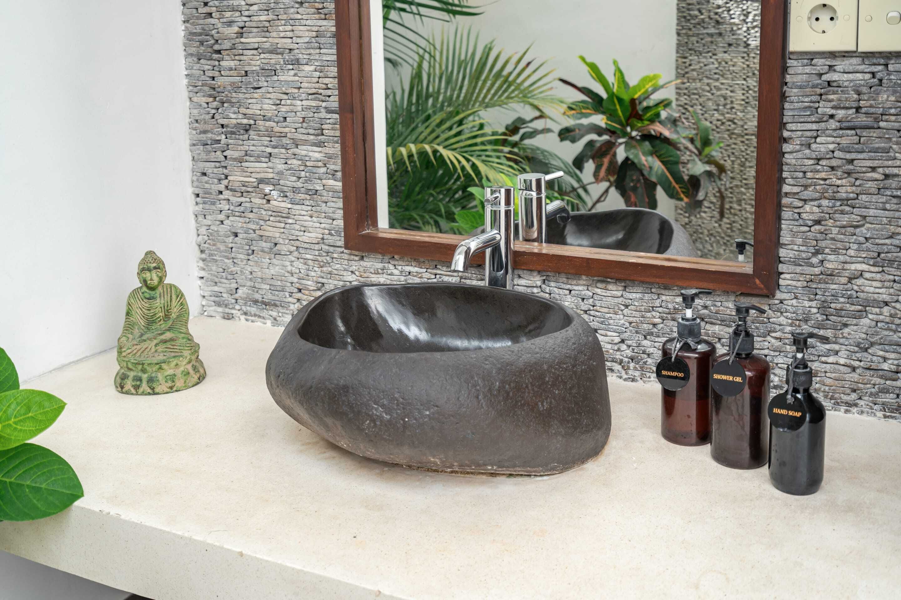 Un baño con lavamanos de piedra, un espejo y artículos de aseo.