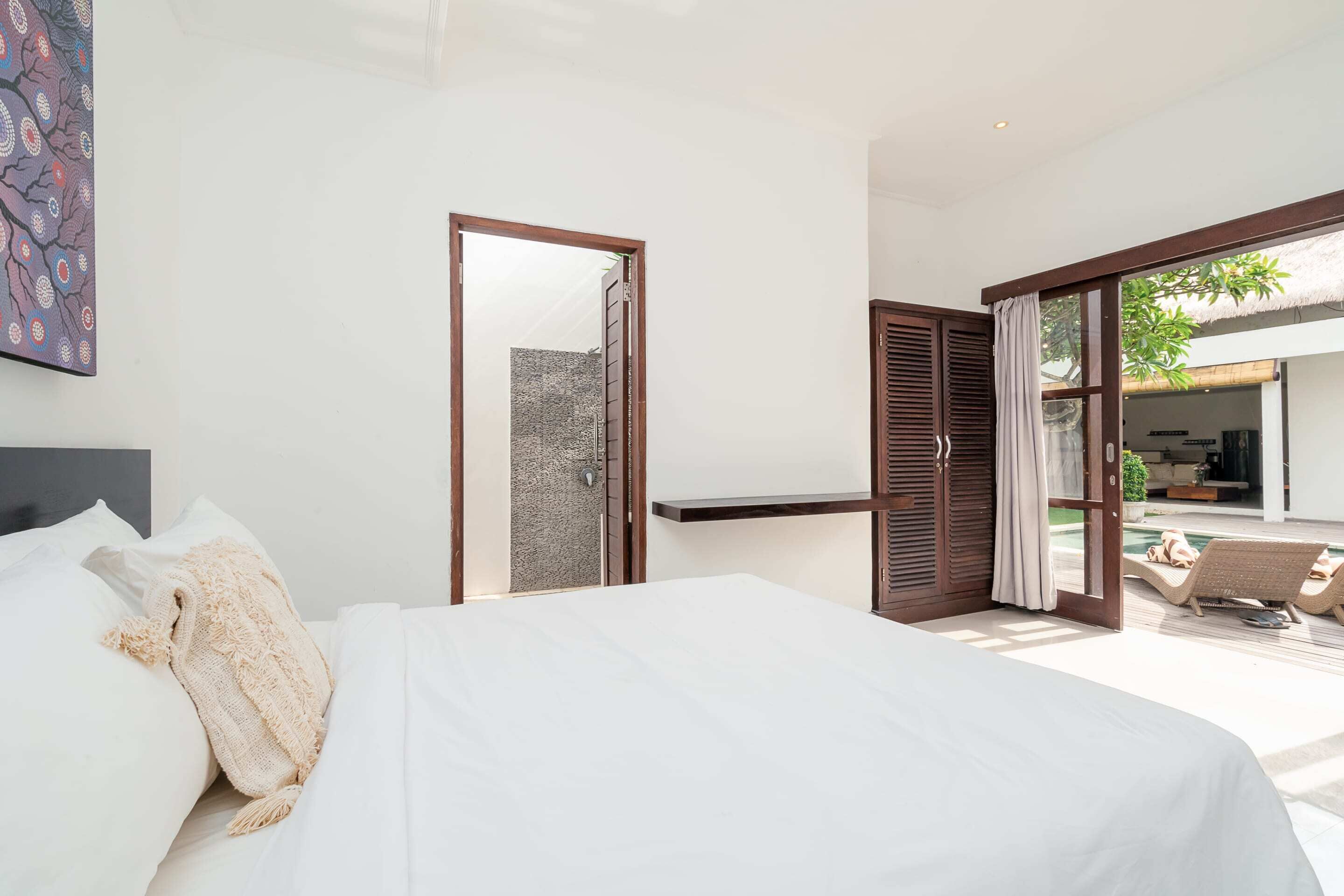 Quarto com uma cama grande, uma porta de madeira que dá para uma varanda e uma pequena prateleira.
