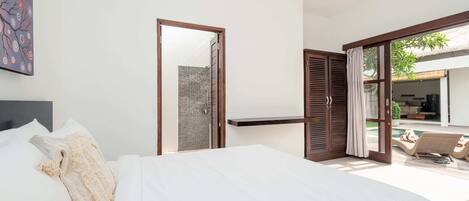 Quarto com uma cama grande, uma porta de madeira que dá para uma varanda e uma pequena prateleira.