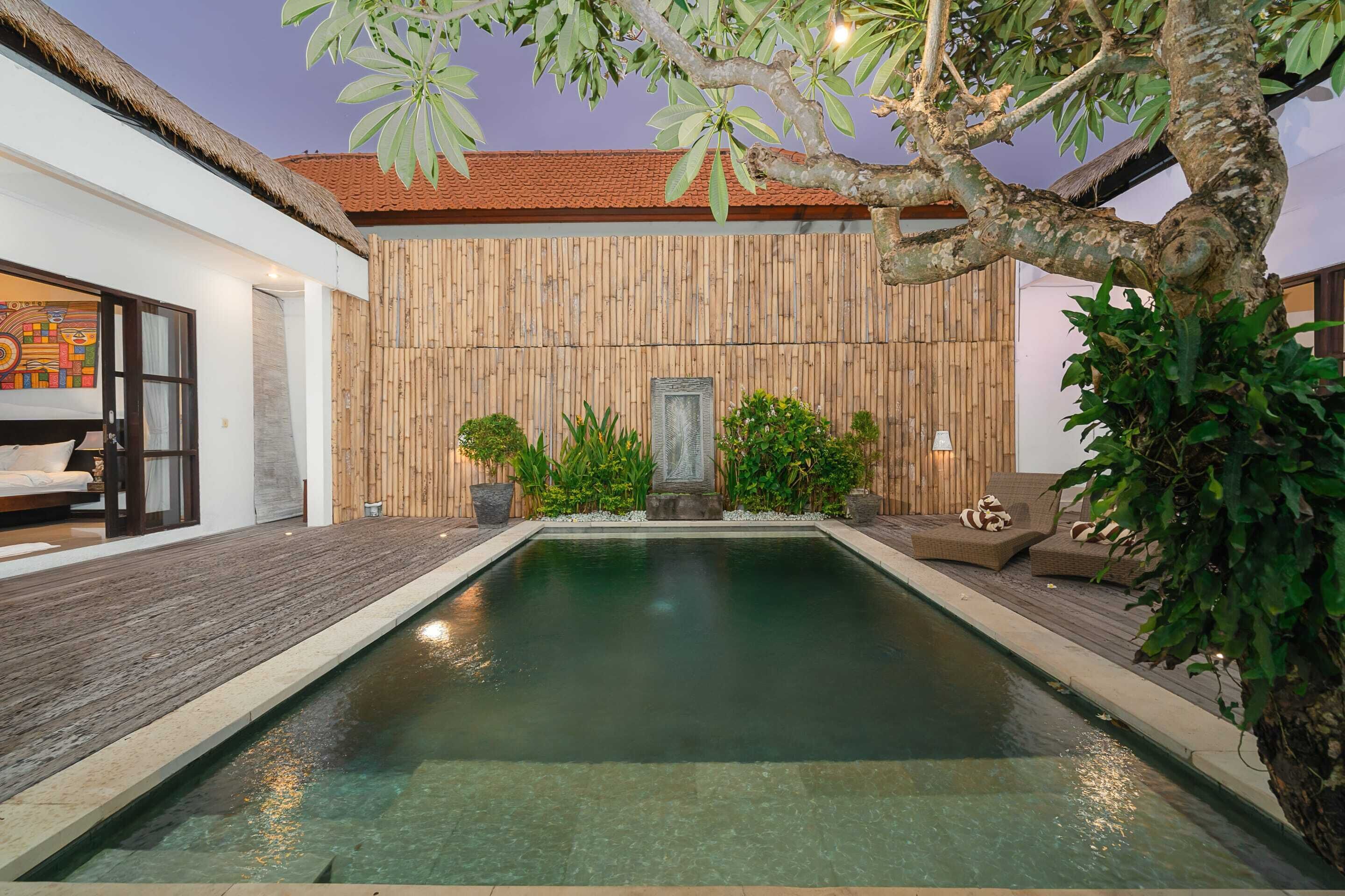 Uma área de piscina com deck de madeira, uma escultura de pedra e assentos externos.