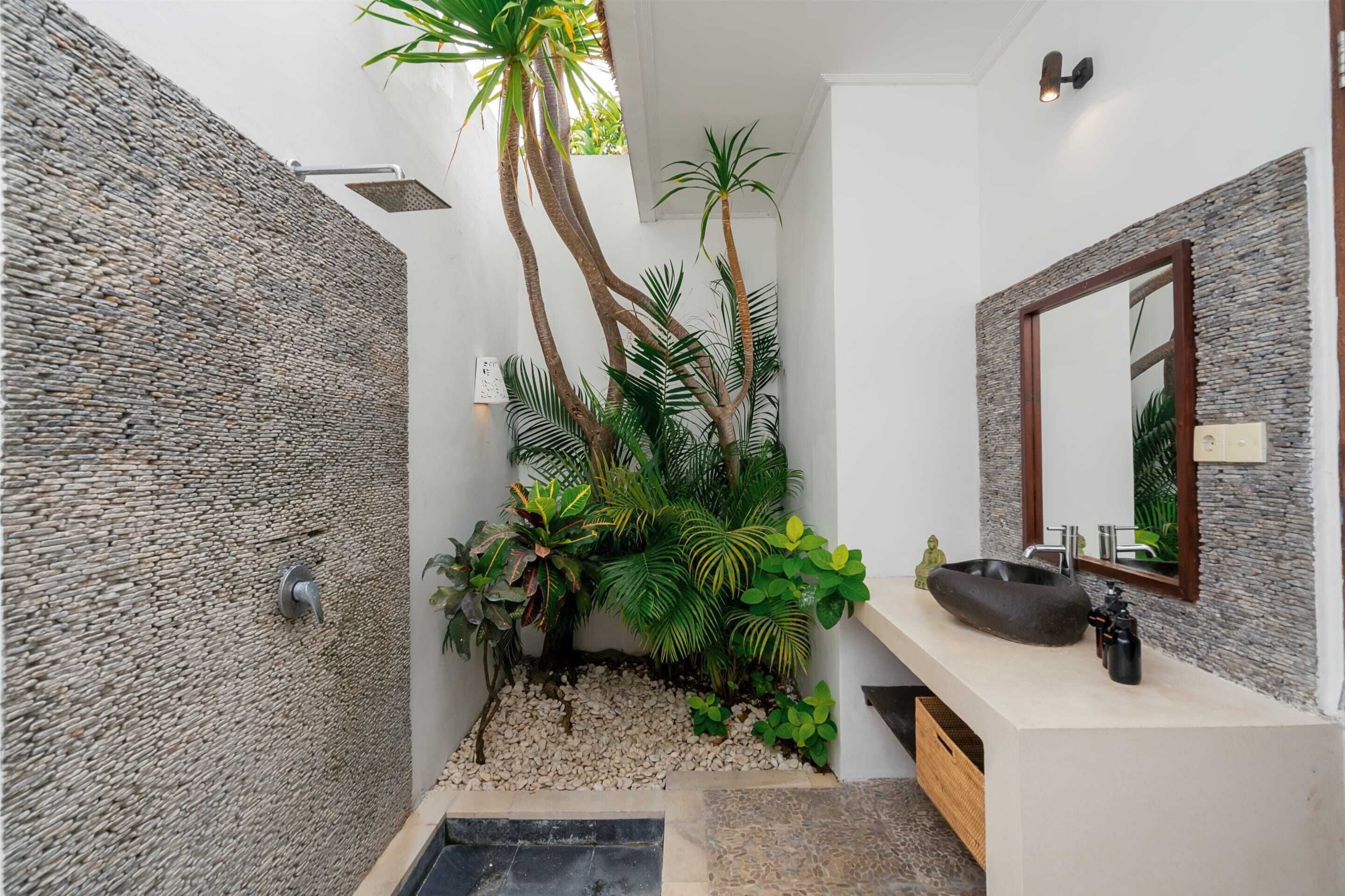 A modern bathroom with a stone wall, a small garden area with plants, a round sink, and a mirror with a stone frame.
