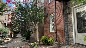 A brick building with a stone-paved courtyard, a small tree, and a window with a door. - Charming Oxford Townhome - Minutes to Ole Miss and The Square!  Sleeps 1-10 (Oxford)