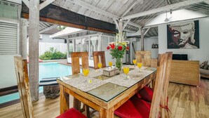 Un comedor con una mesa de vidrio, sillas rojas con cojines y vistas a una piscina.