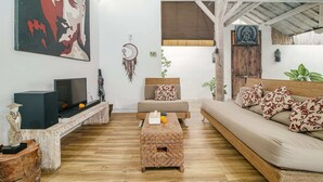 Una sala de estar con un sofá, una mesa de centro, un televisor y un atrapasueños en la pared.