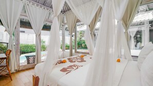 Una cama con dosel, vista a una piscina al aire libre y un comedor con mesa y sillas.