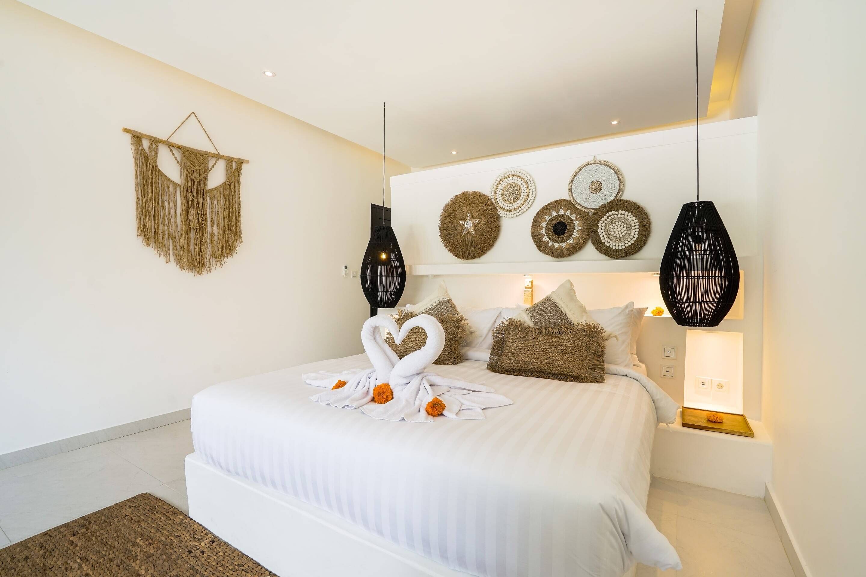 A modern bedroom with a large bed, decorative wall hangings, and two black pendant lights.