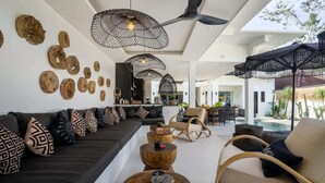Una sala de estar moderna con sofá, mesa de centro y sillones. Cuenta con un ventilador de techo y decoración mural.
