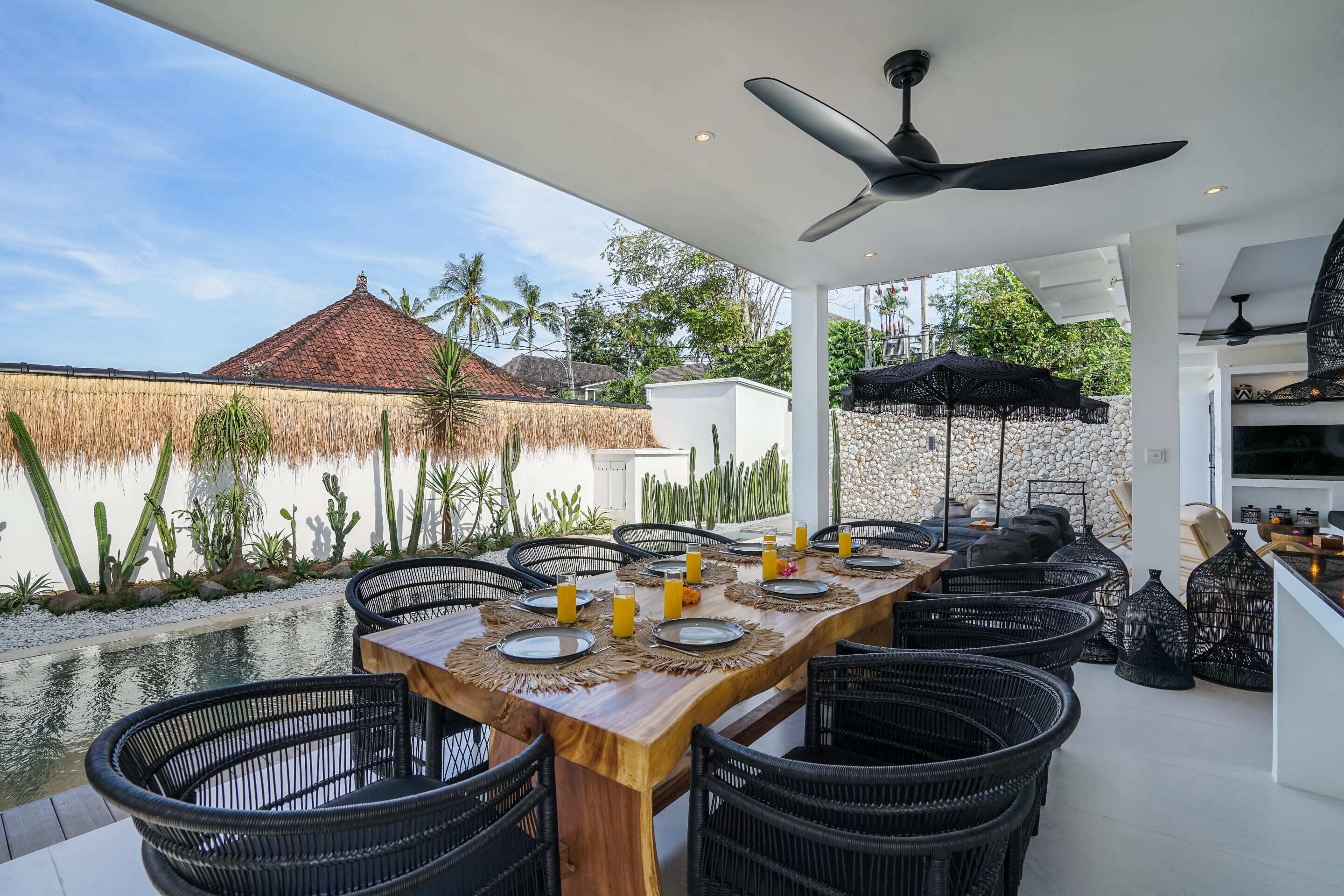 An outdoor dining area with a long wooden table set for six, surrounded by black wicker chairs.