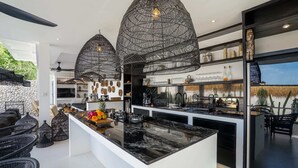 Una cocina moderna con una isla central, lámparas colgantes de estructura metálica negra y una pared de piedra.