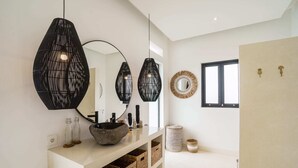 Un baño moderno con un espejo grande, lámparas colgantes negras, un lavabo de piedra y cestas de mimbre.