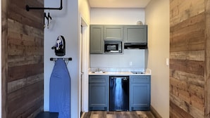 A compact kitchen with wooden walls, a built-in microwave, and a dishwasher. - The Residency Suites (Sugar Land)