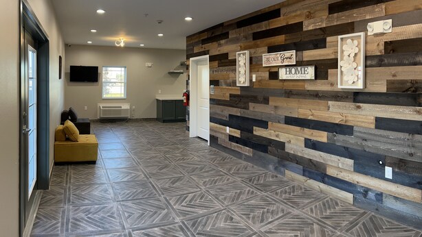 A hallway with a geometric patterned floor, a wooden wall with framed signs, and a yellow sofa. - The Residency Suites (Sugar Land)