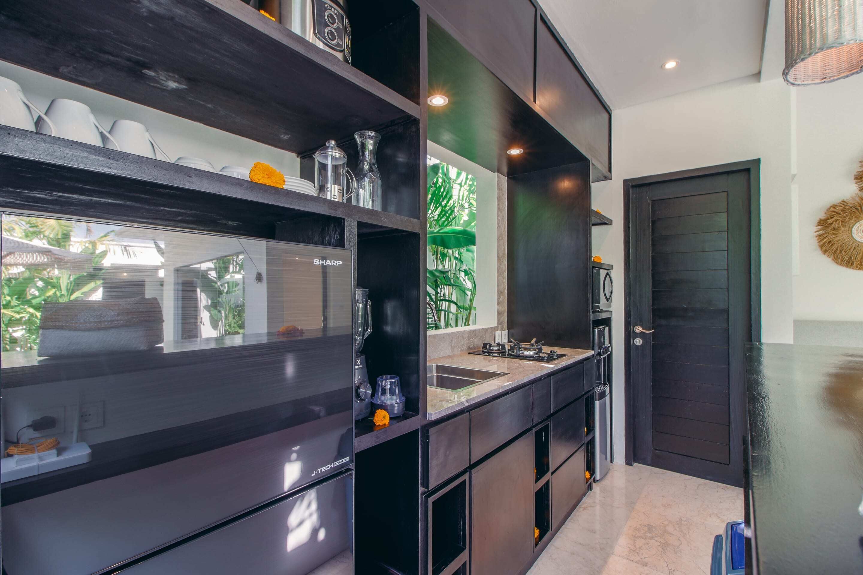 A modern kitchen with dark cabinetry, a built-in oven, and a large window overlooking greenery.