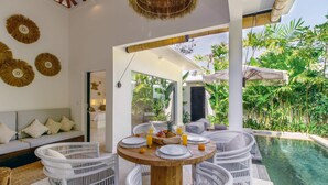 Uma área de refeições ao ar livre moderna, com móveis de vime, uma mesa redonda de madeira e vista para a piscina.