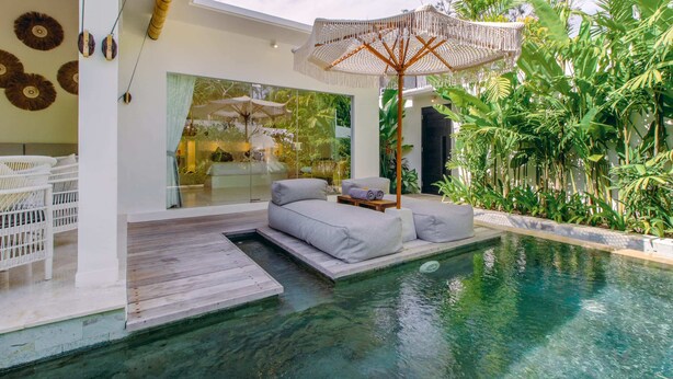 Uma área de piscina moderna ao ar livre, com espaço para sentar, um guarda-sol grande e vegetação exuberante.