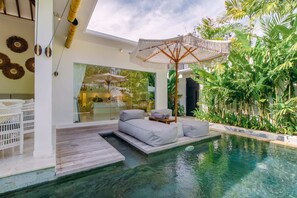 Uma área à beira da piscina com um conjunto de assentos e um muro de vidro que oferece vista para o exterior.