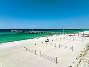 A beach with a long pier extending into the ocean, sandy beach, and volleyball nets.