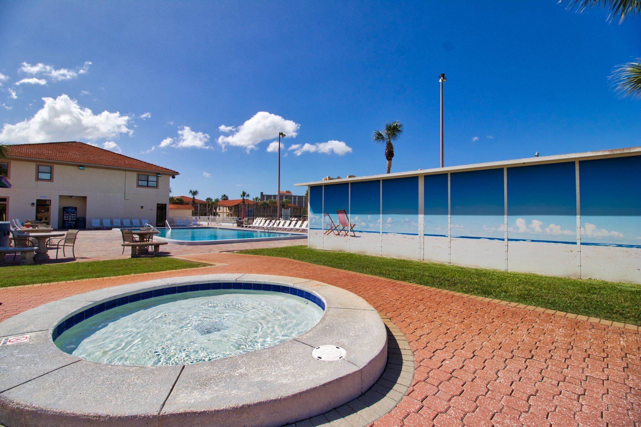 Un área de piscina con un jacuzzi, sillones de descanso y un edificio con tejado de azulejos.
