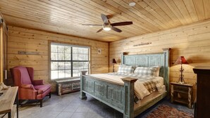 Un dormitorio de cabaña de madera con una cama, una silla, una mesa y un ventilador de techo.