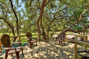 Une terrasse en bois, agrémentée de chaises et de tables, entourée d’arbres.